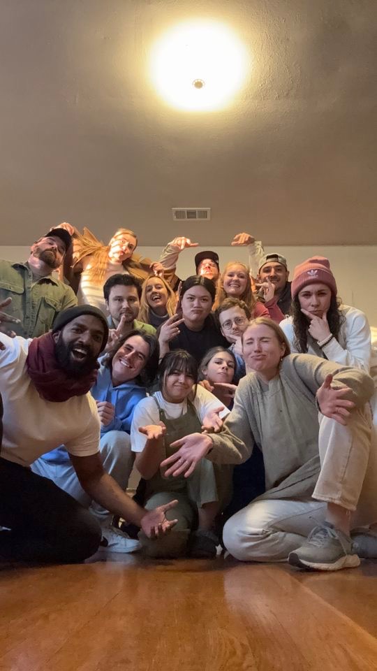 Group of people posing indoors with a ceiling light above, some making gestures, smiling, and looking at the camera.