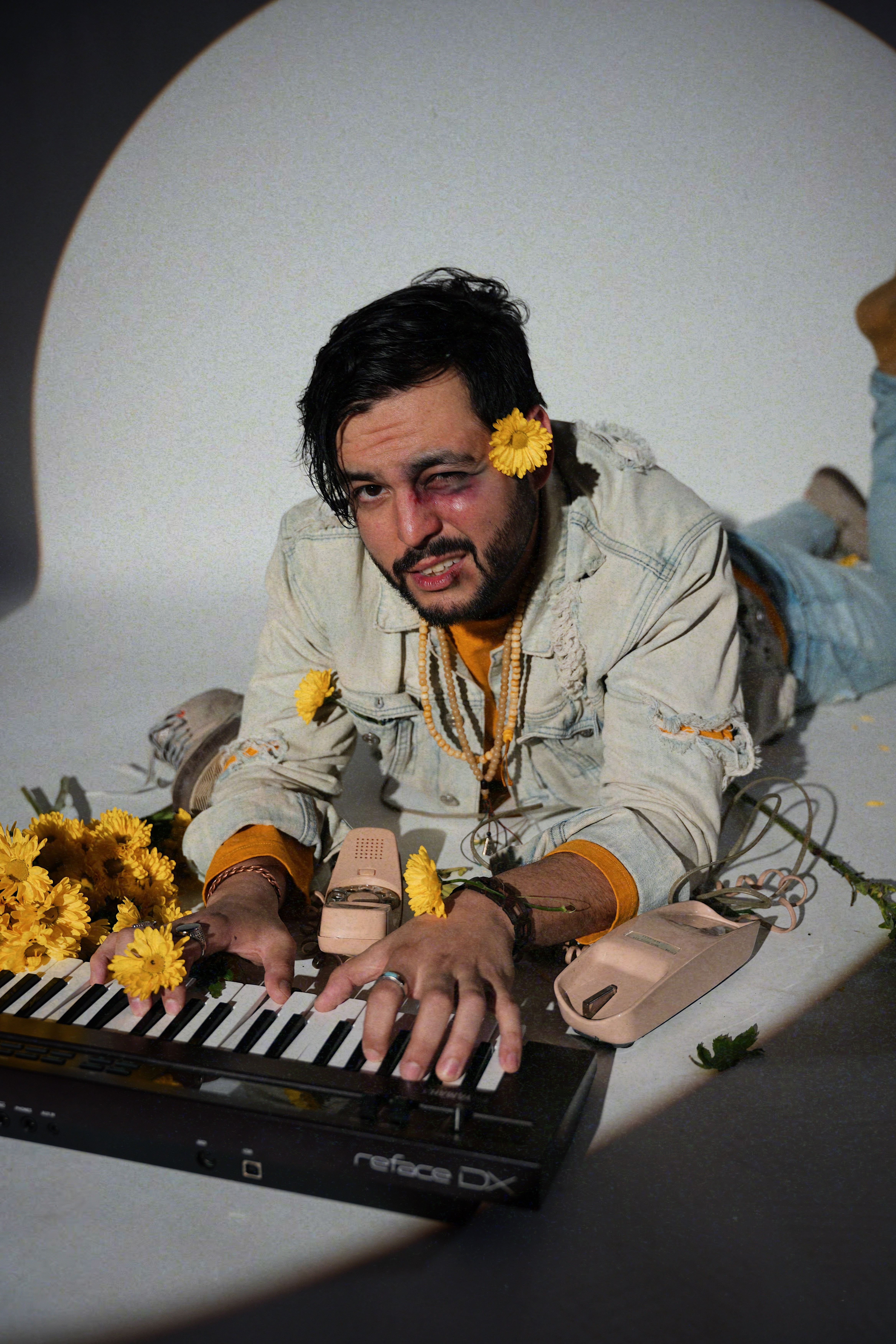 Person lying on the floor playing keyboard, surrounded by yellow flowers, with a plain background.