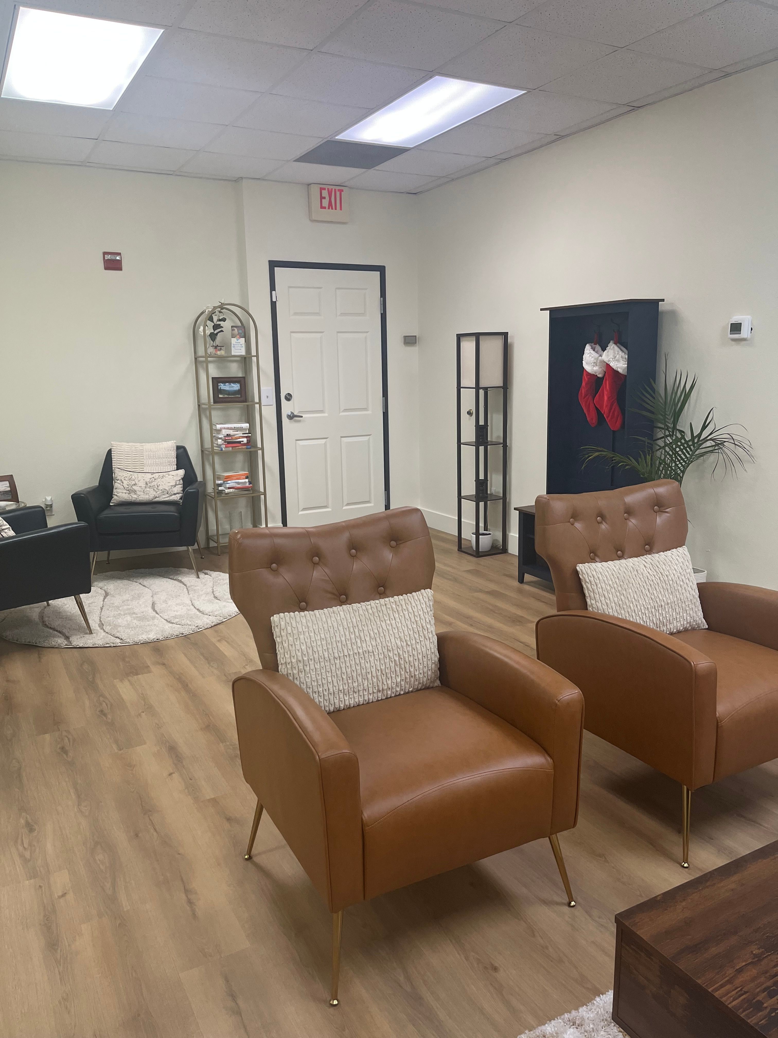 Waiting area with two brown armchairs, a small table, and a black cabinet with a plant inside.