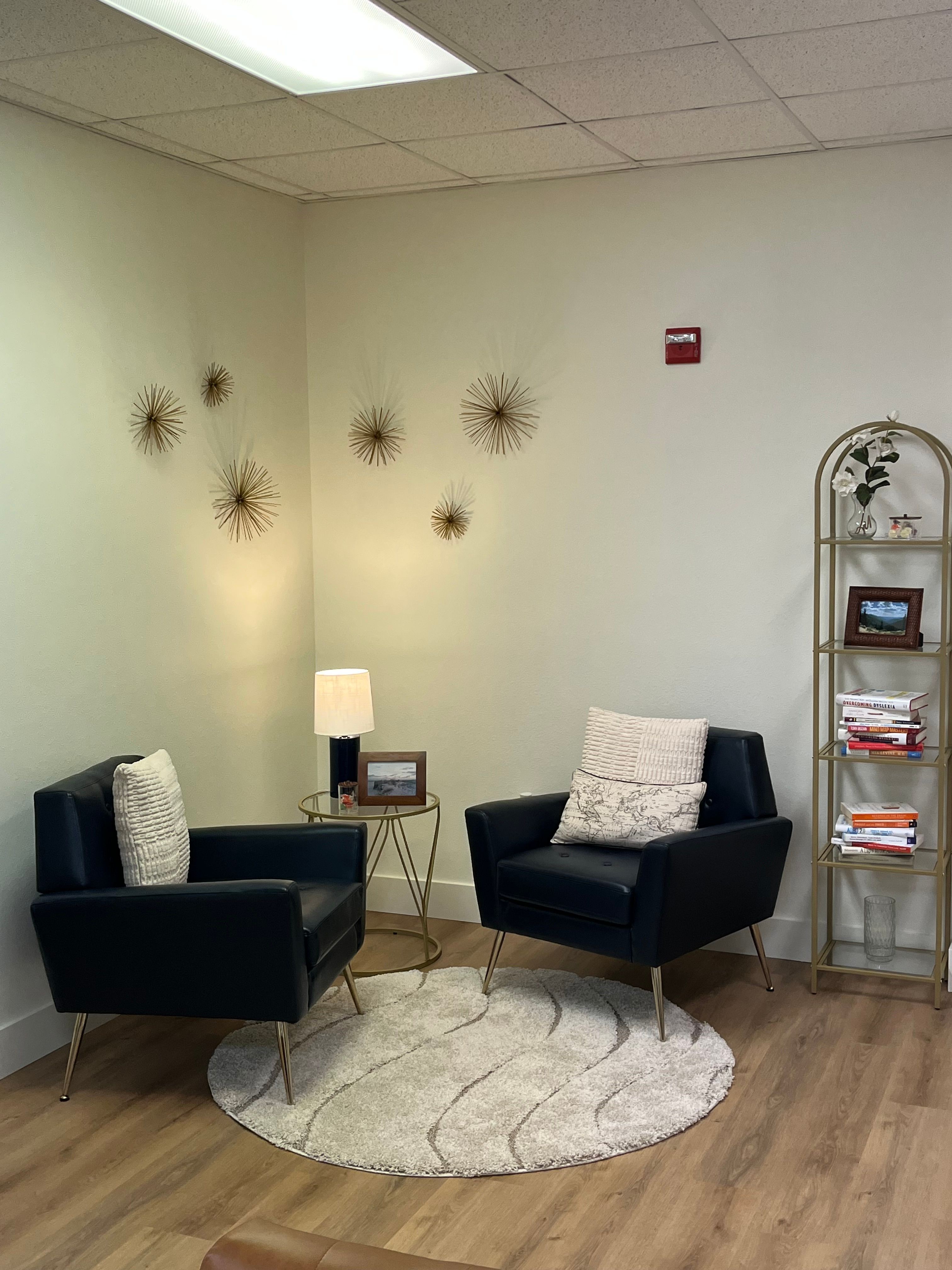 Living room with two black armchairs, a round rug, a bookshelf, and decorative wall art.