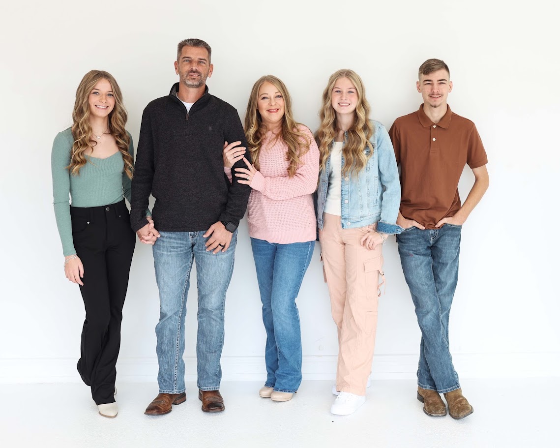 Group of five people standing together against a white background, smiling, with arms linked or by their sides.