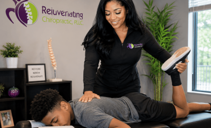 Chiropractor smiling while adjusting a patient's leg during a consultation in a clinic room.