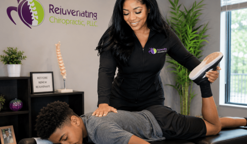 Chiropractor smiling while adjusting a patient's leg during a consultation in a clinic room.