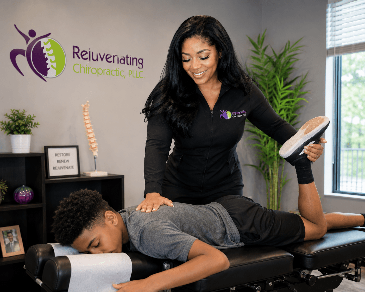 Chiropractor smiling while adjusting a patient's leg during a consultation in a clinic room.
