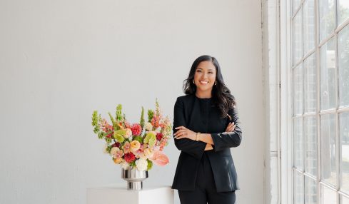 Woman in black suit standing next to a flower arrangement in a bright room with large windows