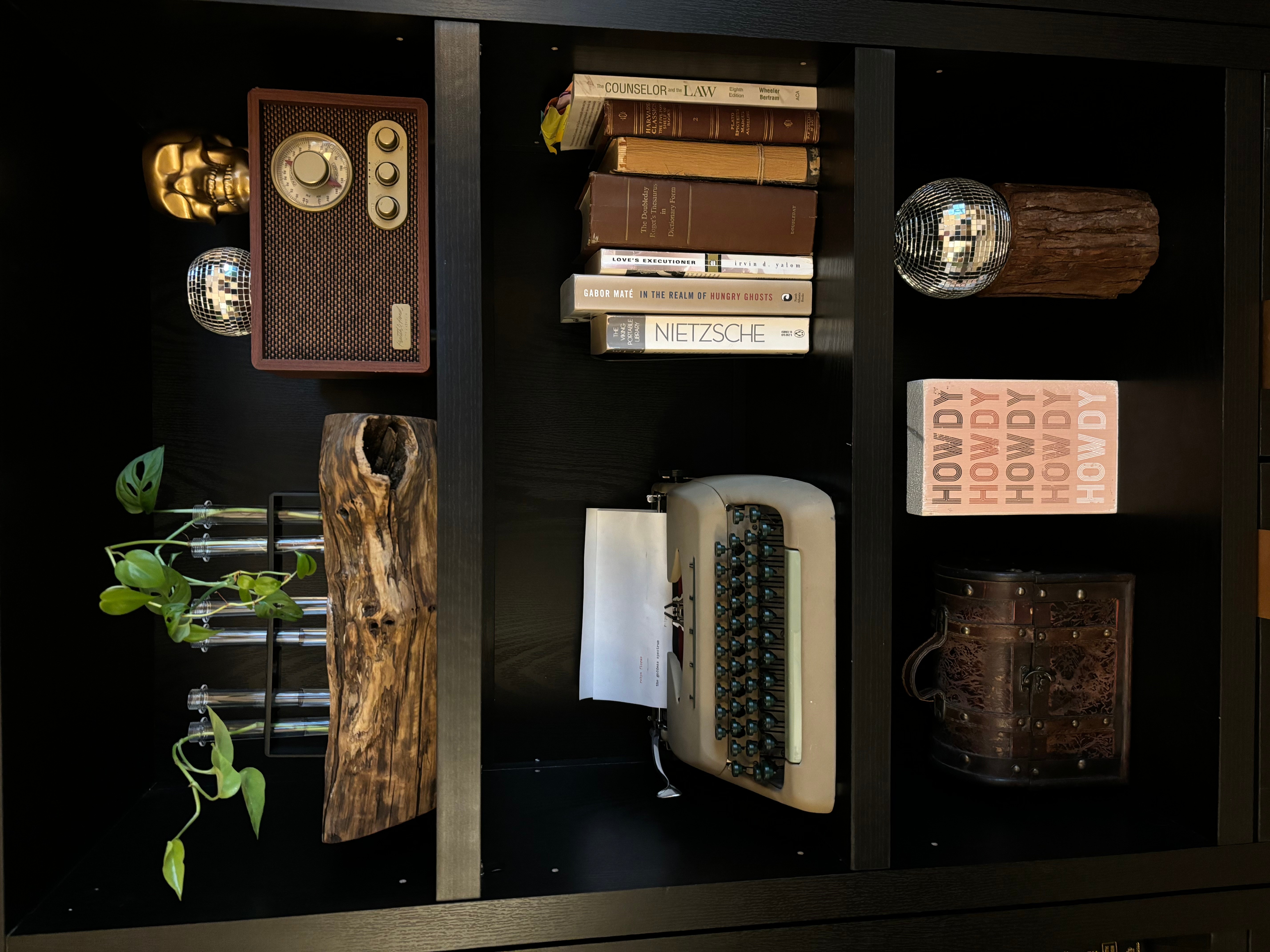 Shelf with vintage radio, books, typewriter, and decorative items, including a plant and wooden objects.
