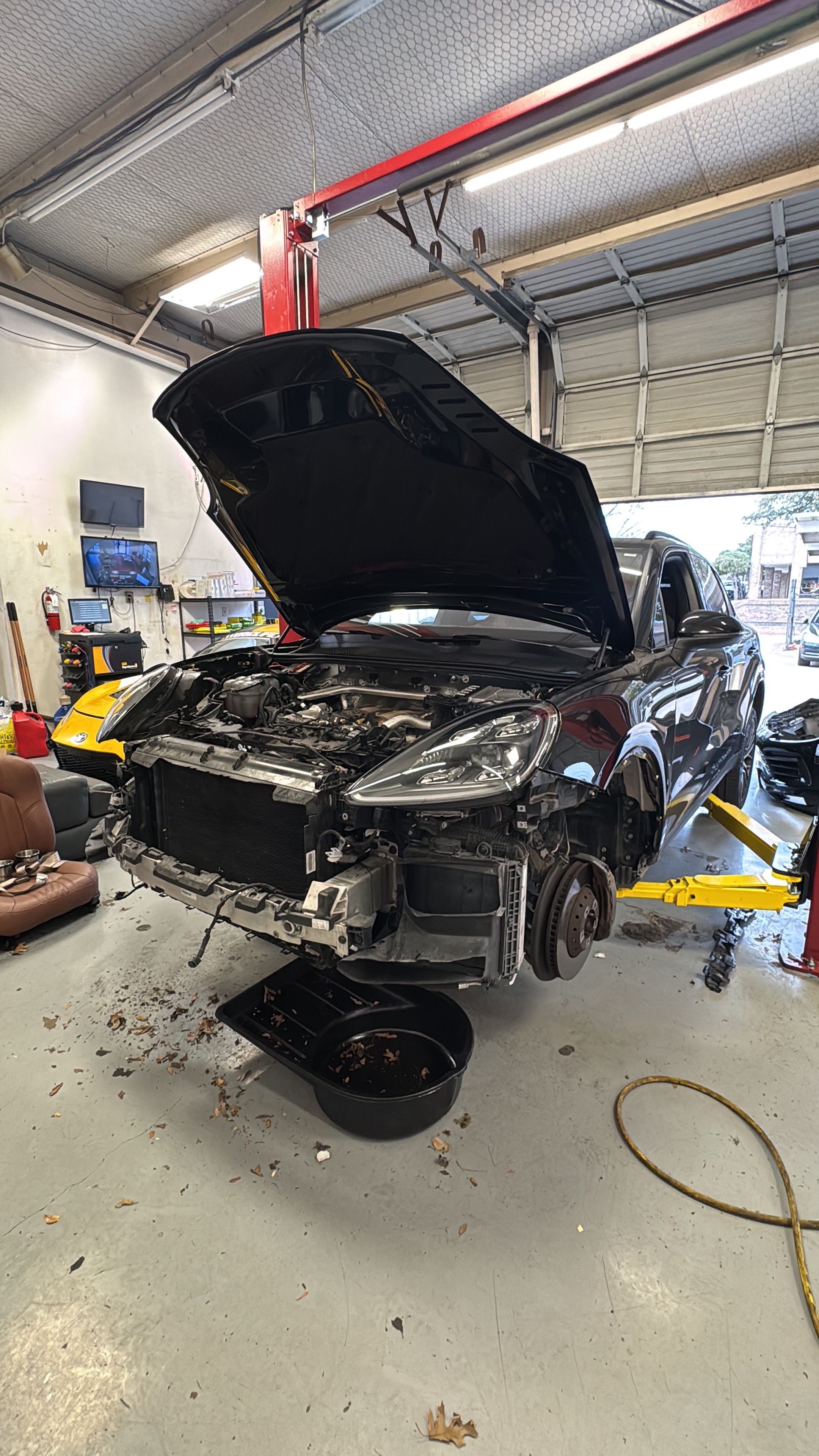 Car with open hood inside a garage, engine exposed, surrounded by tools and equipment.