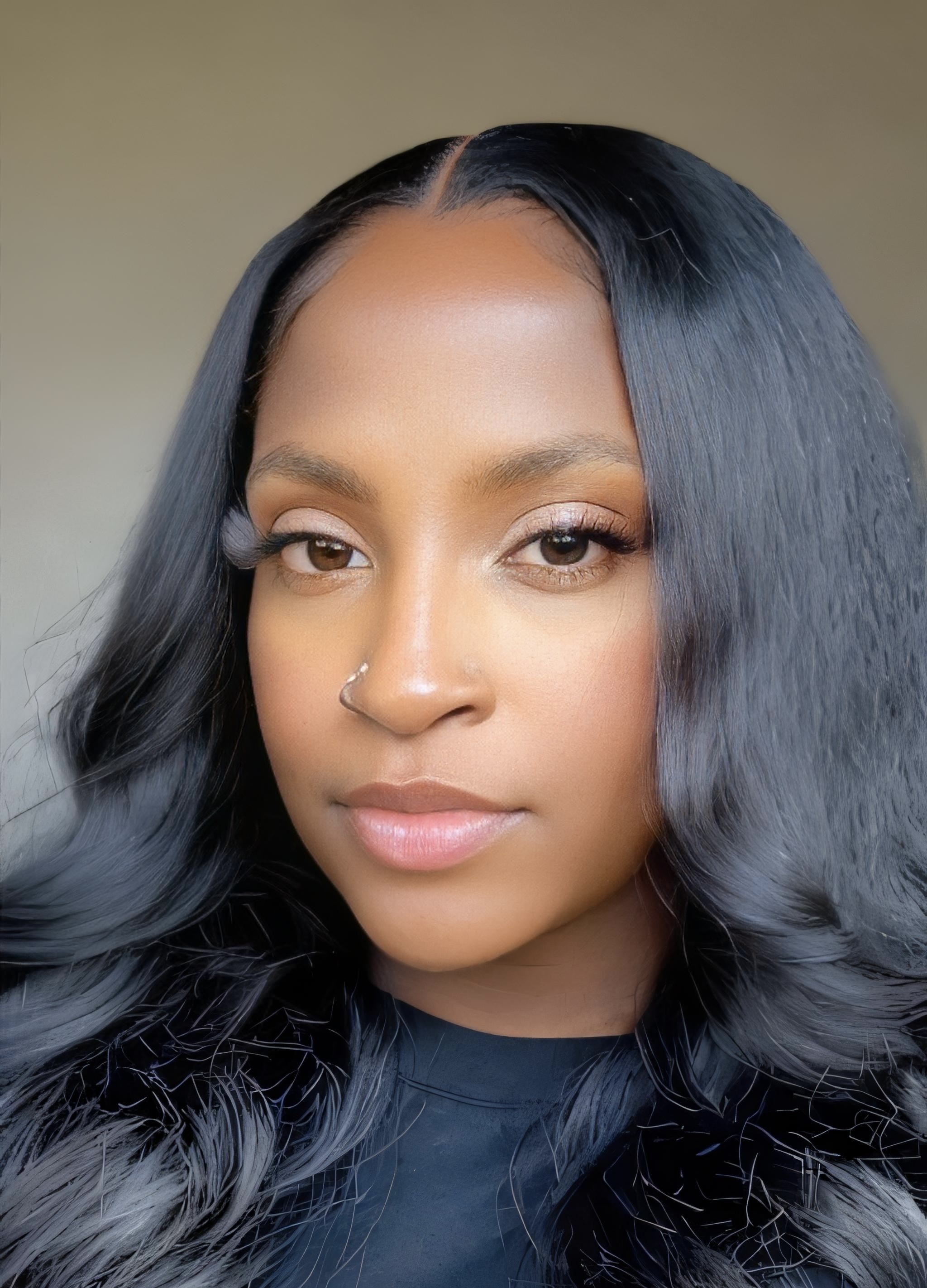 Close-up portrait of a woman with long, wavy black hair and a nose piercing, looking directly at the camera.
