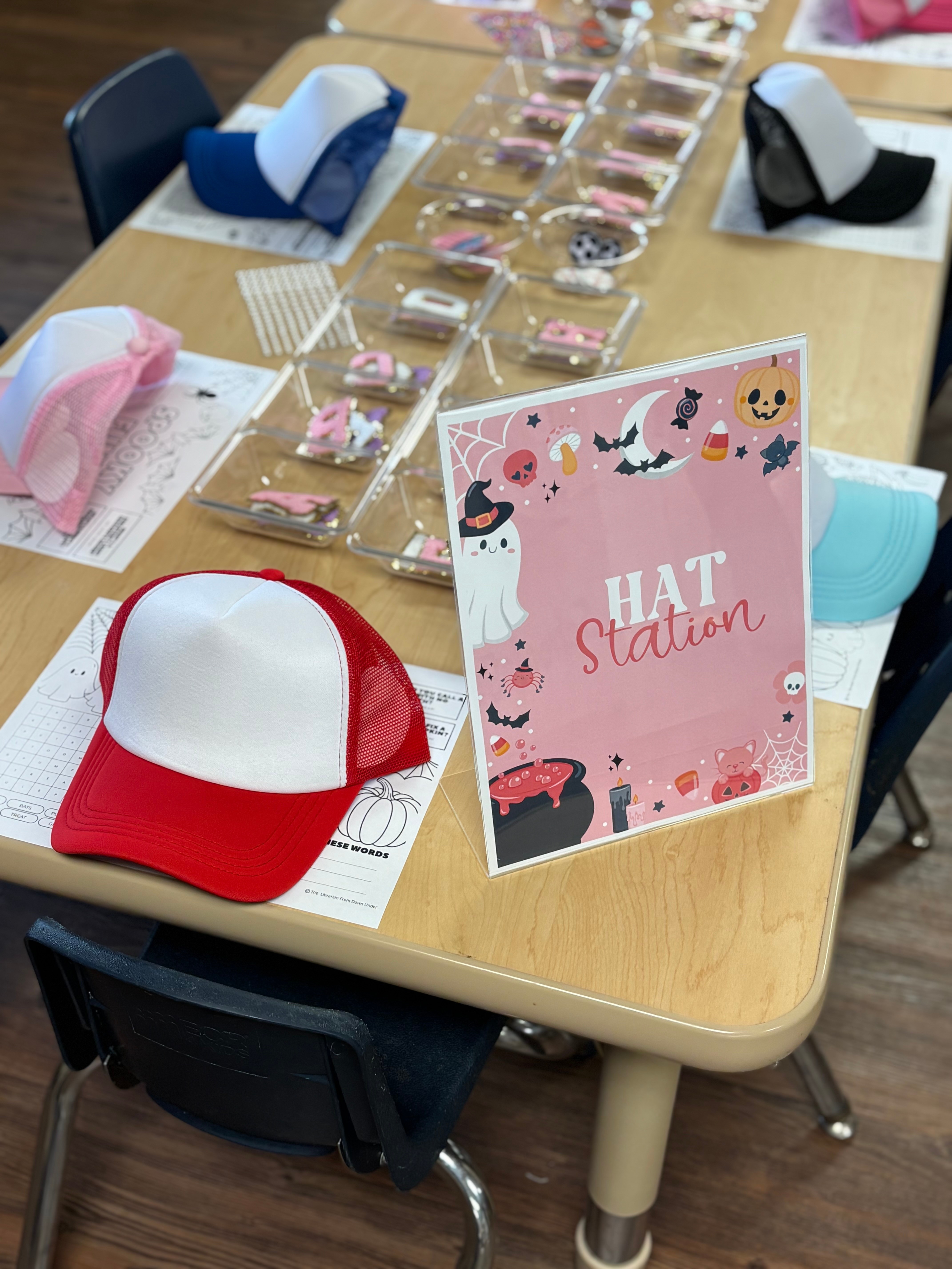 Table with pink, red, and blue hats, and a pink sign reading 'HAT Station' with illustrations of hats and animals.