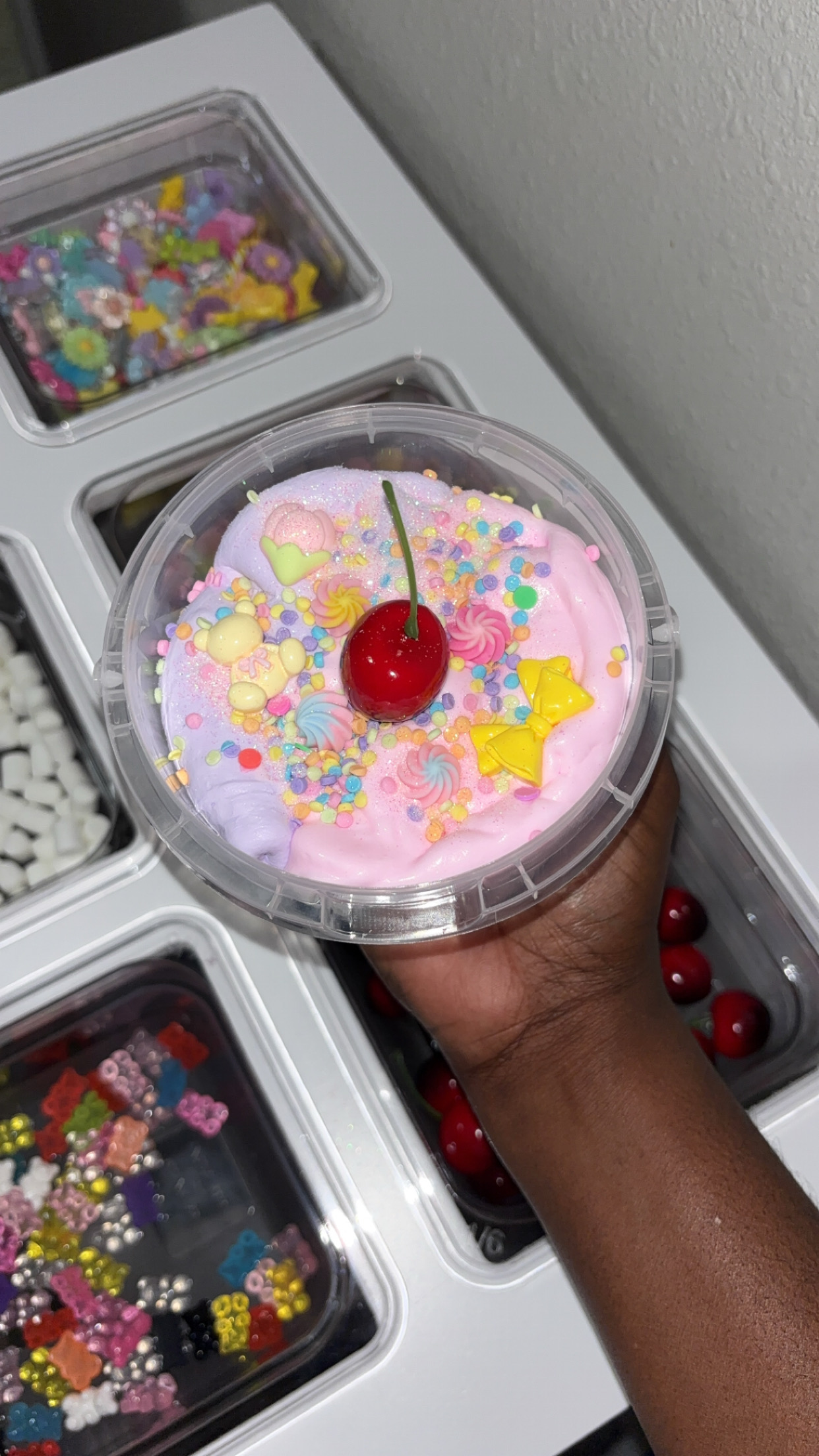 Person holding a pink frosted cupcake with colorful sprinkles, a yellow star, and a cherry on top.