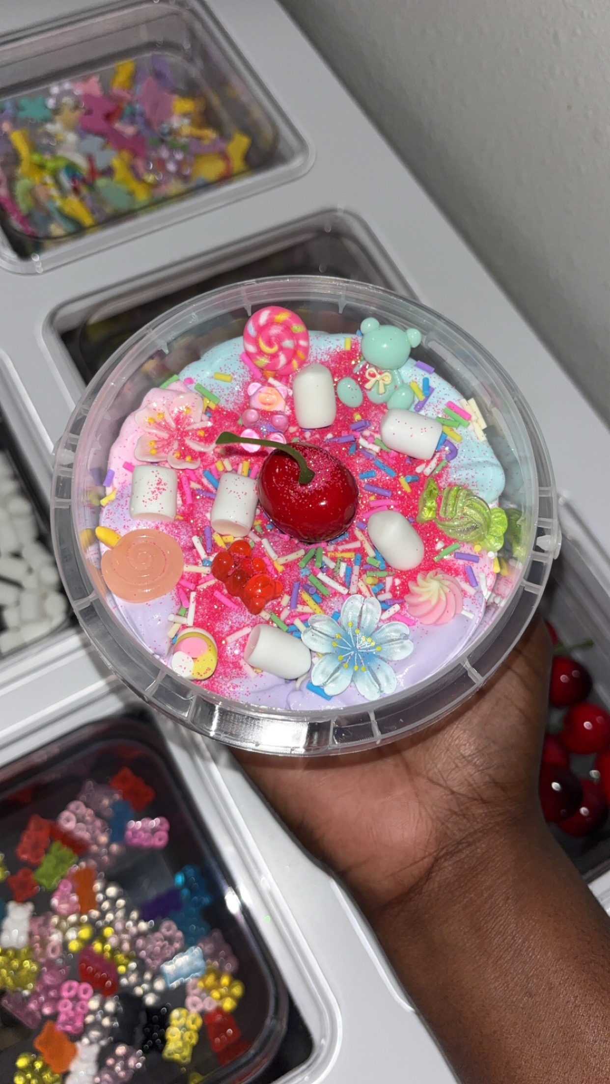 Hand holding a container filled with colorful candies and a cherry on top.