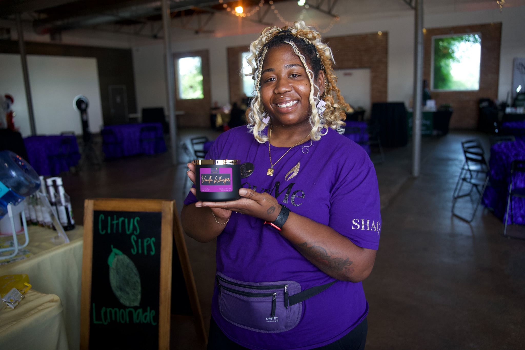 Smiling woman holding a small box in a decorated event space with tables and a chalkboard sign.