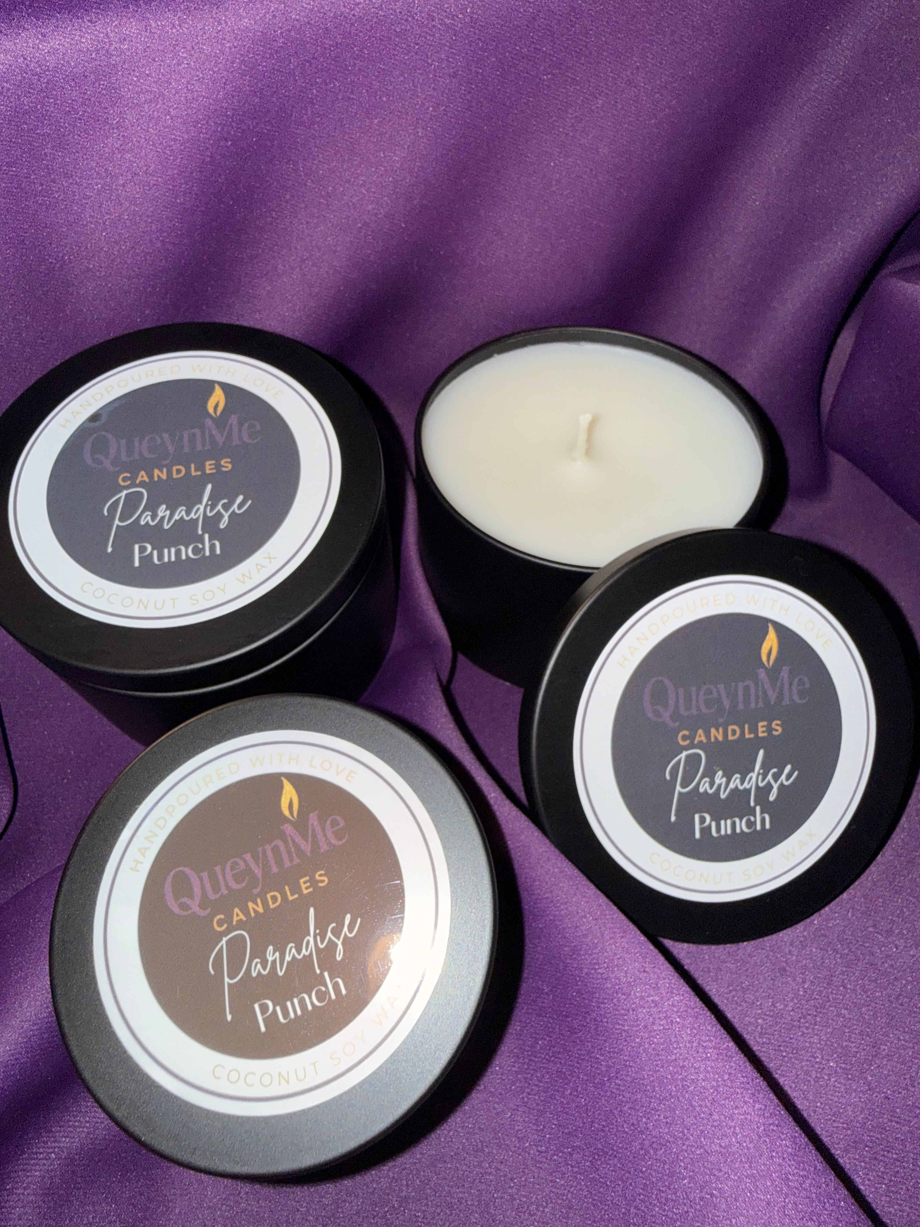 Three black containers of scented candle with purple labels on purple satin fabric.