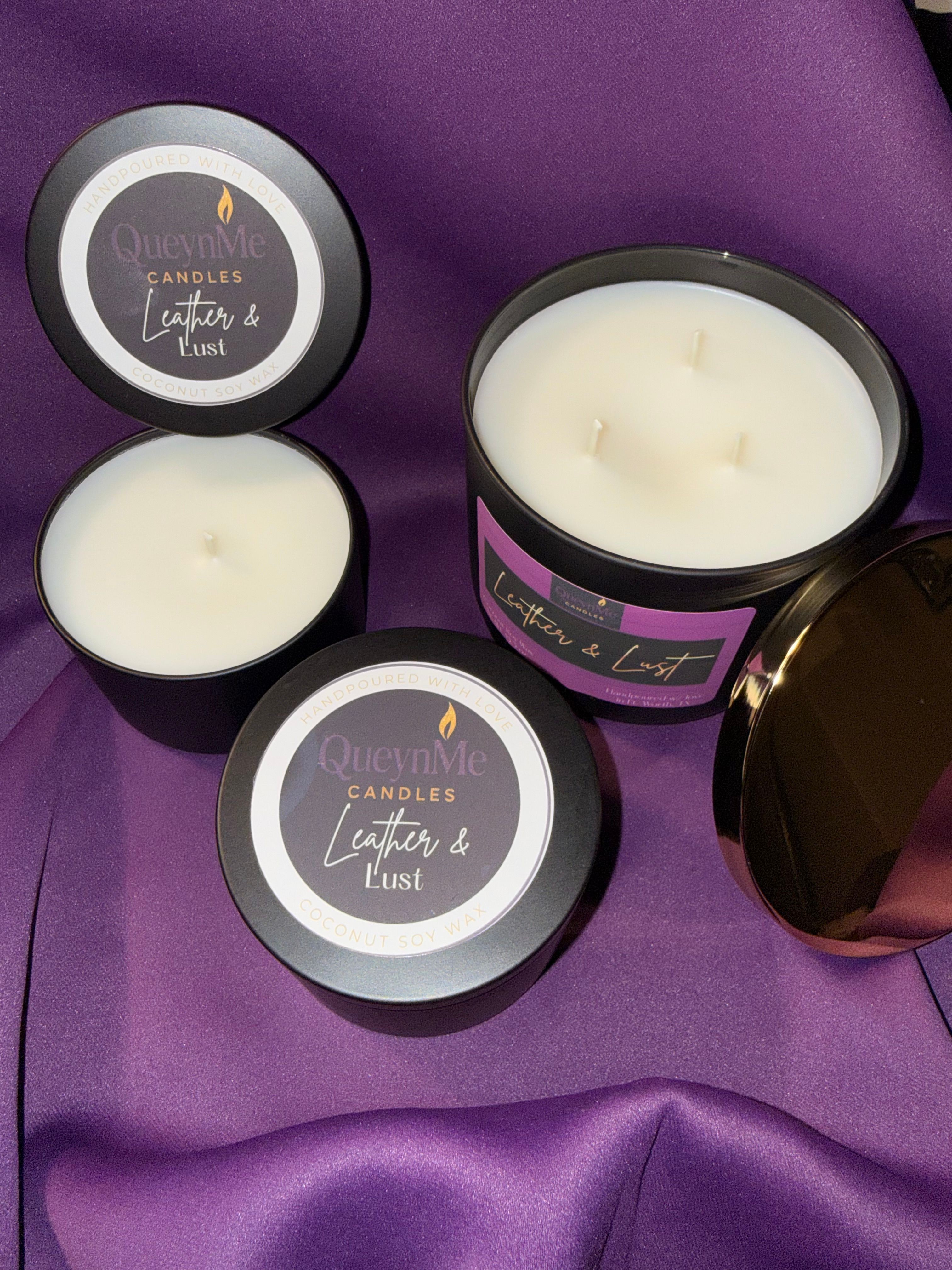 Three black containers with white candles on purple fabric, one open showing the candle inside, and a brown jar in the background.