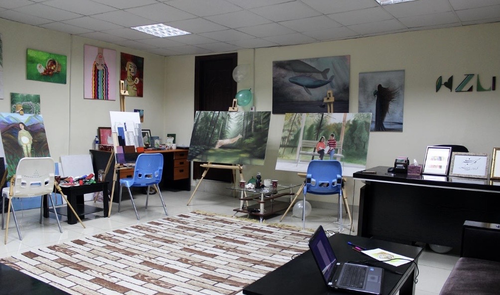 Art gallery with paintings on walls and tables, chairs, and a rug on the floor.