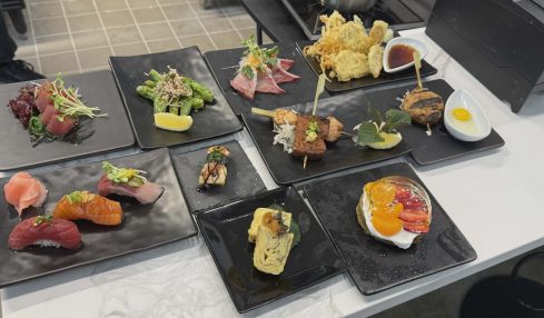 Assorted Japanese dishes including sashimi, tempura, and sushi on black plates, arranged on a white table.