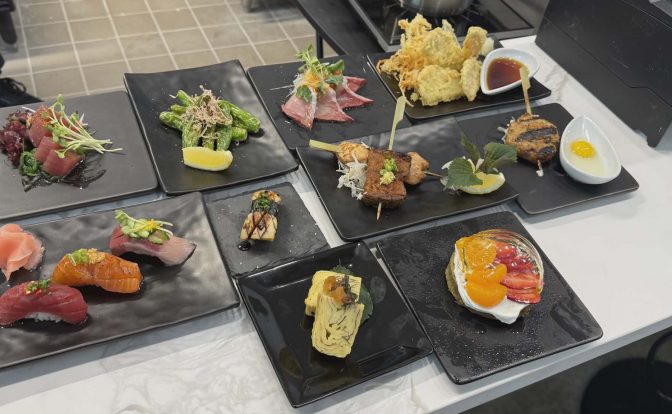 Assorted Japanese dishes including sashimi, tempura, and sushi on black plates, arranged on a white table.