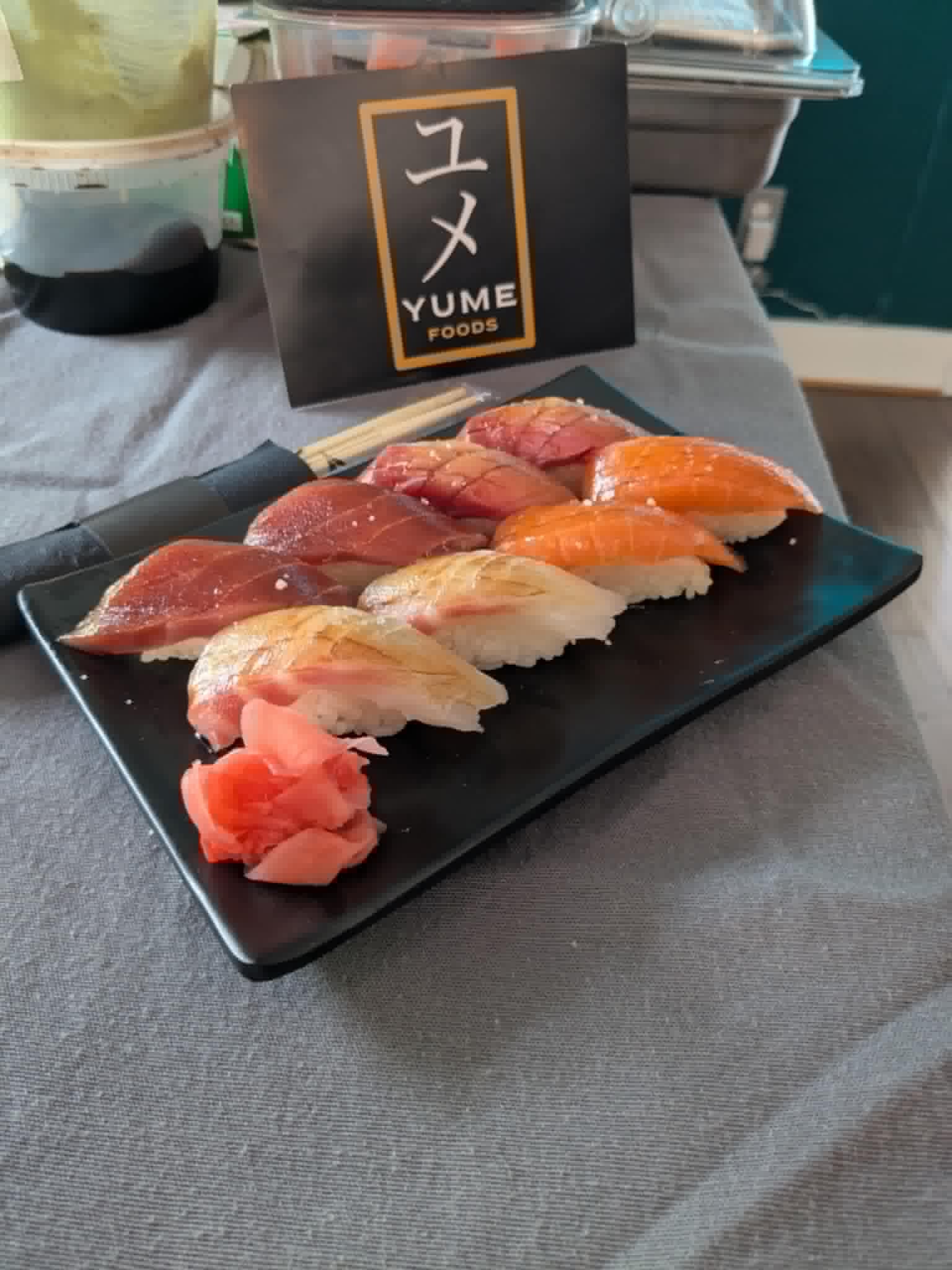Assorted sushi pieces on a black rectangular plate with a small mound of pink pickled ginger, placed on a gray table.