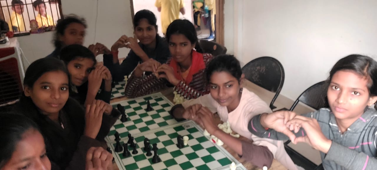 Group of children playing chess at a table indoors, some smiling and looking at the camera.